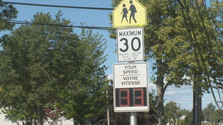 A school zone sign shows a 30 km/hr speed limit above an automated speed checker.