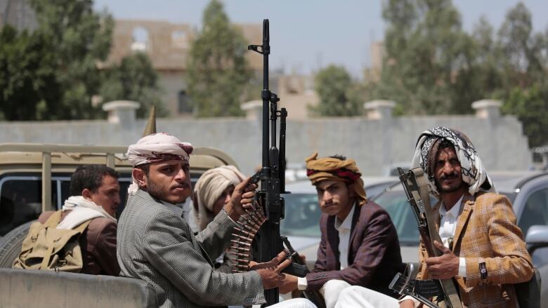 Five men, some armed with large machine guns, sit in the back of a pickup truck. 