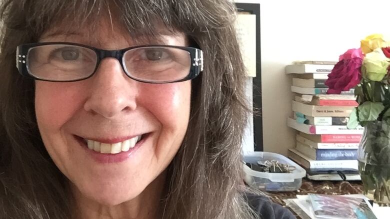 Smiling woman with grey hair and glasses with a pile of books in the background