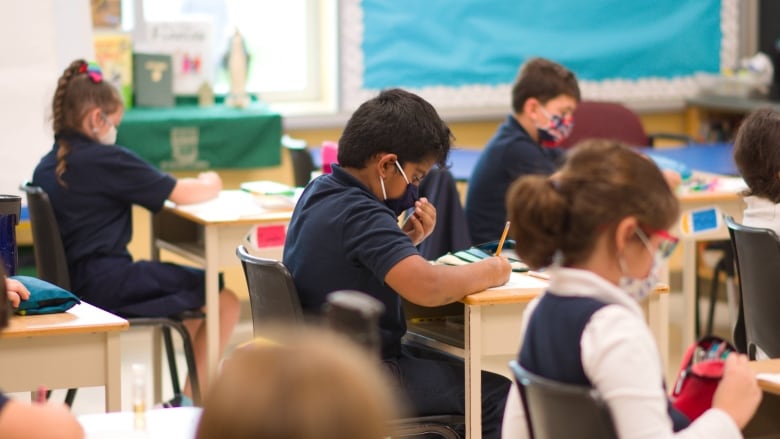 Children sit at classroom desks wearing masks.