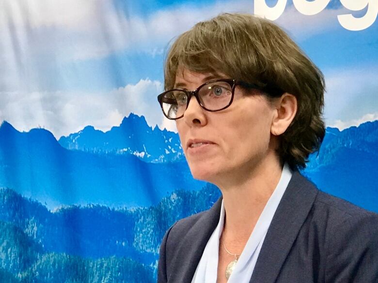 Sonia Furstenau, the leader of the Green Party, wears a suit jacket as she stands in front of a backdrop photo of mountains.