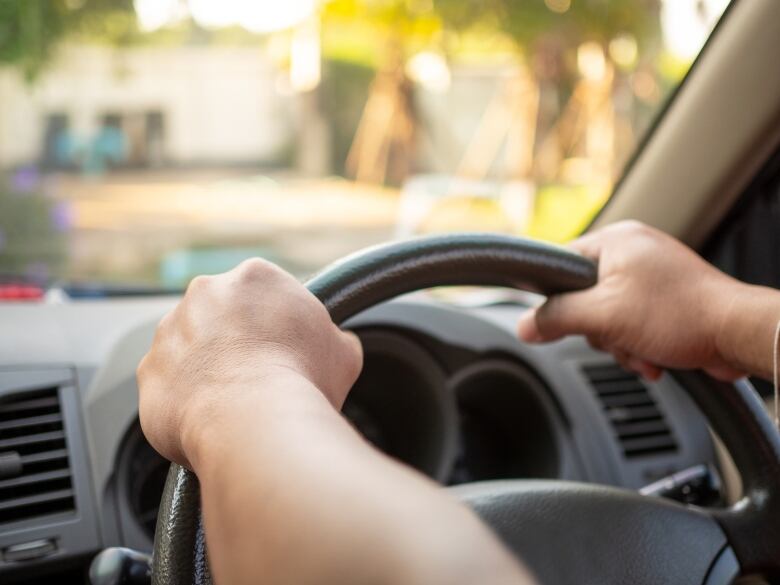 Two hands grip a car steering wheel.