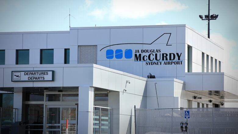 A sign on the outside of an airport building shows a picture of an airplane and the name J.A. Douglas McCurdy Sydney Airport.