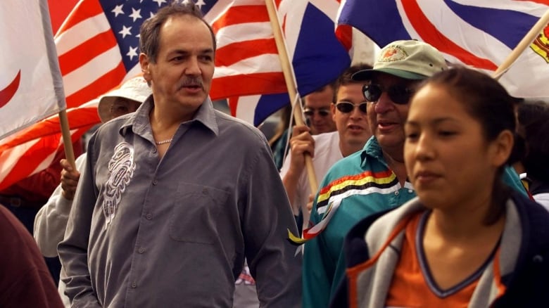 People stand together during a protest, holding up flags in the background.