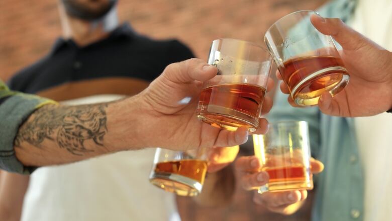 A group of hands toasting glasses together in the sunlight.