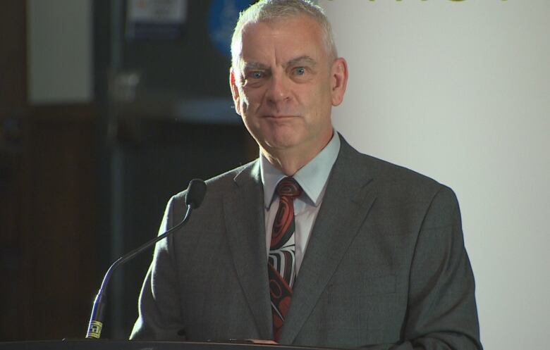 A man wearing a grey suit standing a podium. 