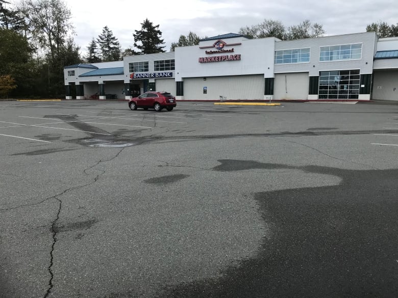 A red car stands alone in an empty parking lot of a Point Roberts grocery store. 