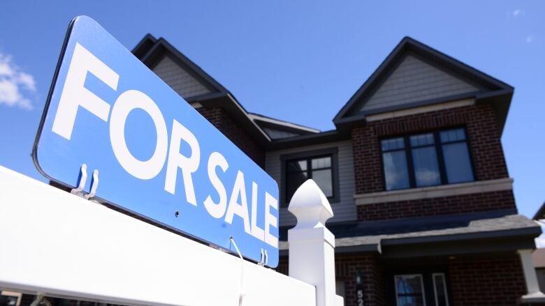 A blue and white for sale sign in front of a red brick house