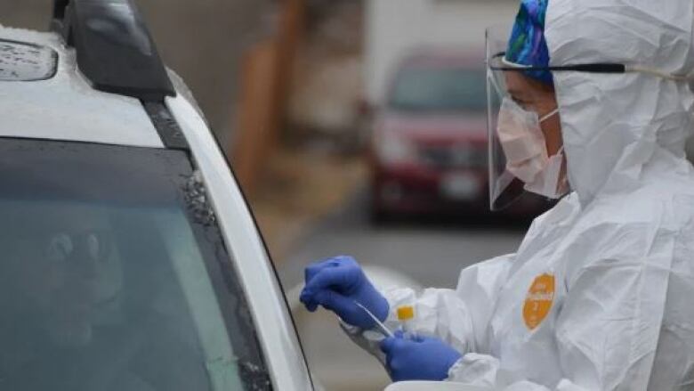 A woman in a white protective suit holds a swab out towards a car