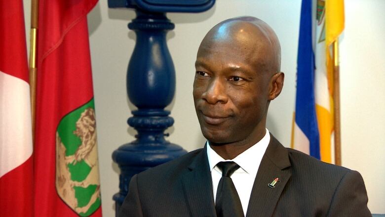 A man in a black suit and tie smiles.