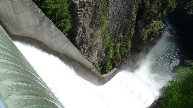 Flowing water off a dam, with spectators visible well in the background.