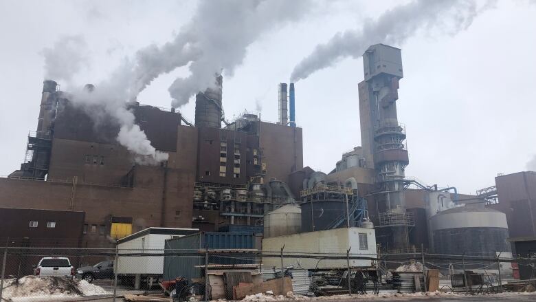 A factory building with several plumes of white gas coming out of pipes