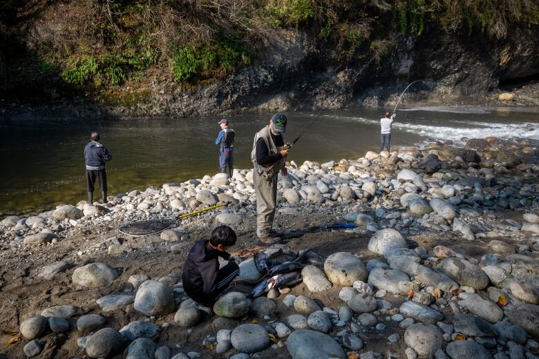 A number of people at a rocky riverbank with fishing rods.