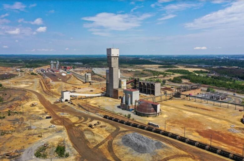 A mine shaft surrounded by mining infrastructure on a large dirt expanse under a blue, sunny sky