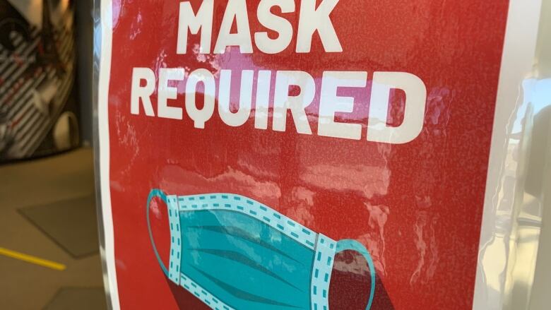 A large red sign shows a picture of a medical mask with the words 'MASK REQUIRED' printed in large bolded white lettering.