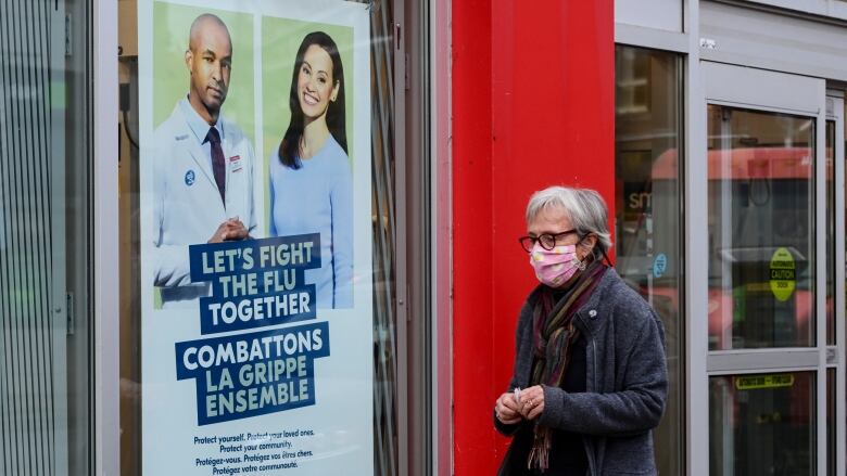 Someone in a light coat and mask walks by a bilingual sign saying 'Let's fight the flu together.'