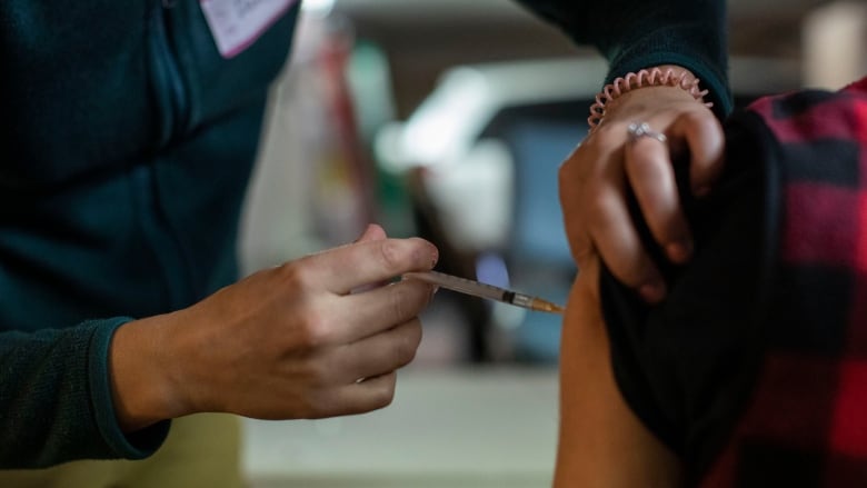 A person administers a vaccine into the arm of another person. 