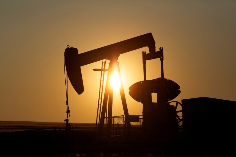 A silhouette of oil pump jack sits on the prairie, with the sun behind. 