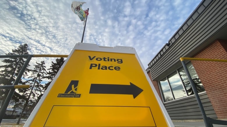 A yellow sign with an arrow under the words 'Voting Place' sits in front of a building.