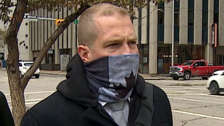 A man walks down the street wearing a black and white mask with the Canadian flag on it. 