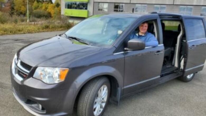 A man sits in the driver's seat of a mini-van.