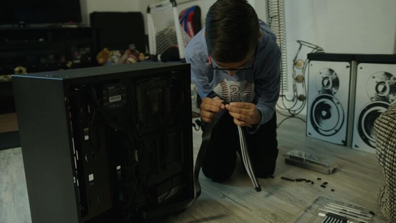 A child sits on the ground next to a computer. They are holding two cables. 