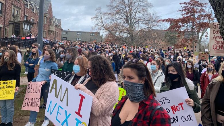 A group of dozens of young people hold handwritten signs. 