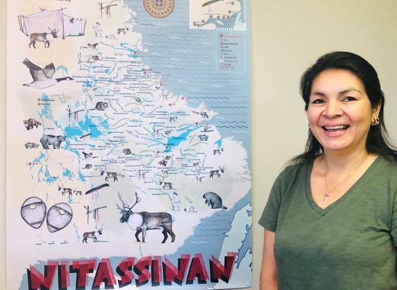 A woman smile at the camera, standing beside a map of Labrador.