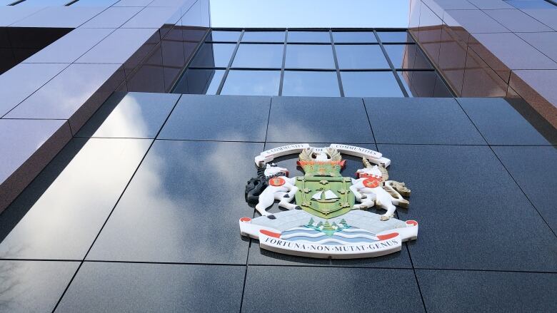 Looking up at the front of a building with a city hall logo, windows and the sky.