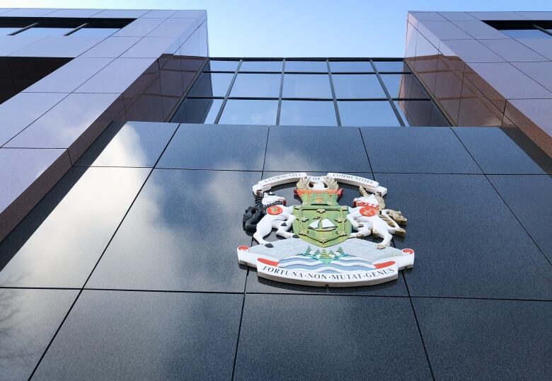 Looking up at the front of a building with a city hall logo, windows and the sky.