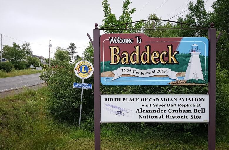 Wooden sign says welcome to Baddeck and has a picture of a lighthouse painted on it.