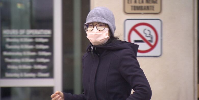 A woman wearing a jacket, hat, medical mask and glasses.