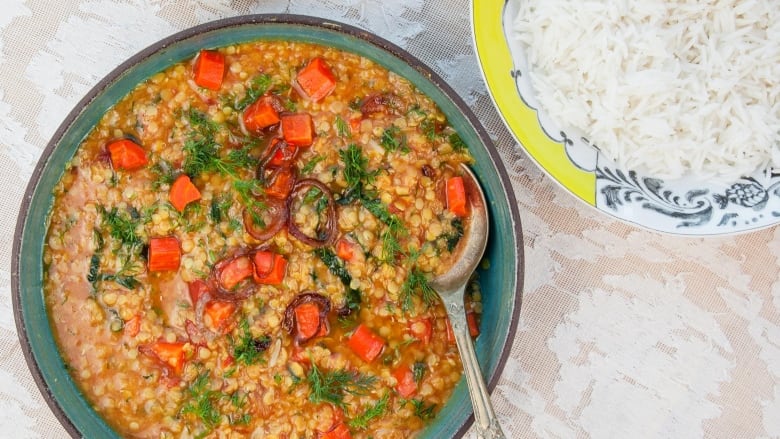 Overhead shot of a green plate of Dal aur Sabzi, Lentils with Roasted Carrots and Kale on a white lace tablecloth. A yellow plate of basmati rice sits next to it. 