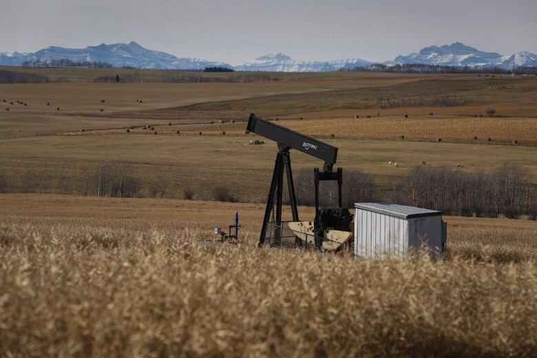 An oil well appears on a prairie field. Mountains are visible along horizon. 