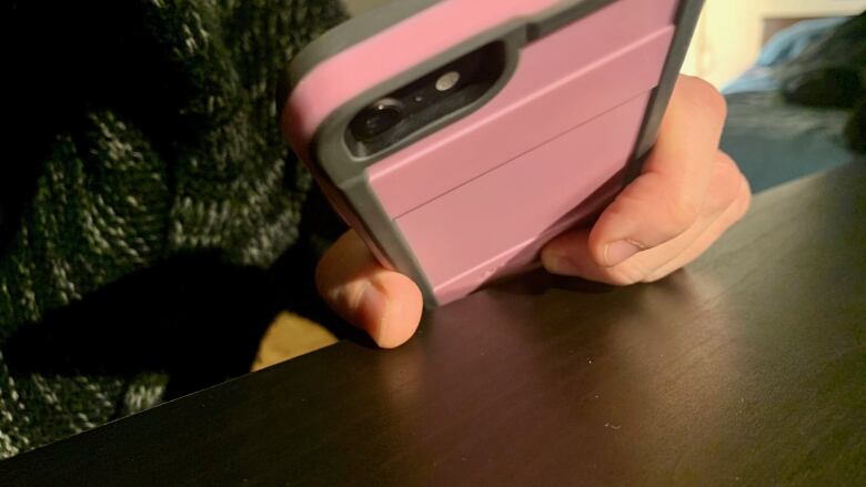 A person holds a smartphone in a pink case with their hand resting on a table.