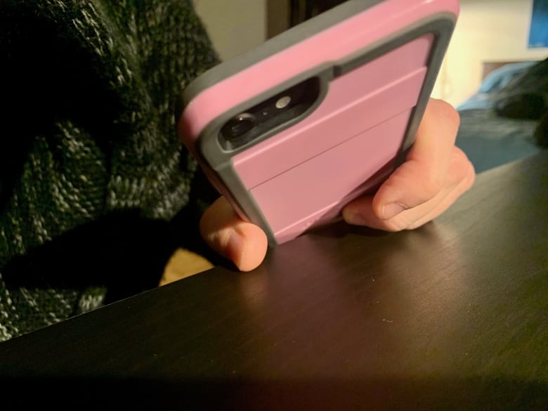 A person holds a smartphone in a pink case with their hand resting on a table.