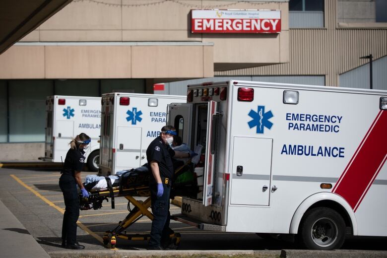 Two paramedics remove a person in a gurney from an ambulance in a parking lot.