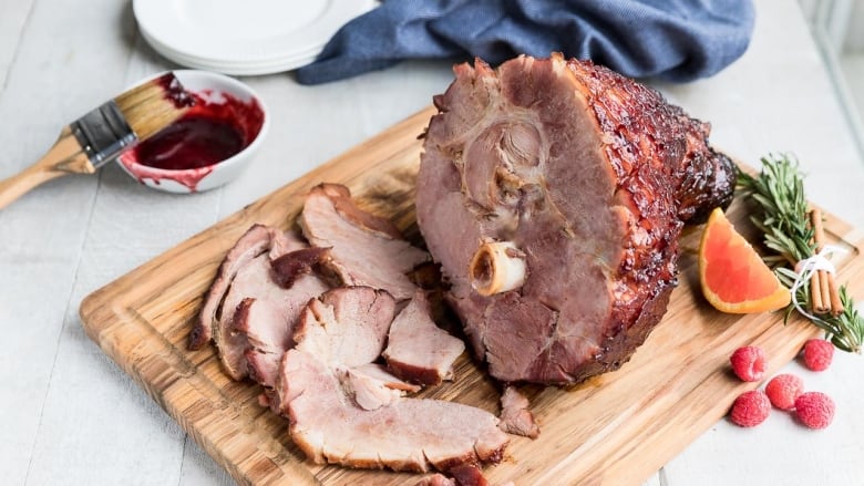 A glazed ham on a wooden cutting board with some slices cut from it. 