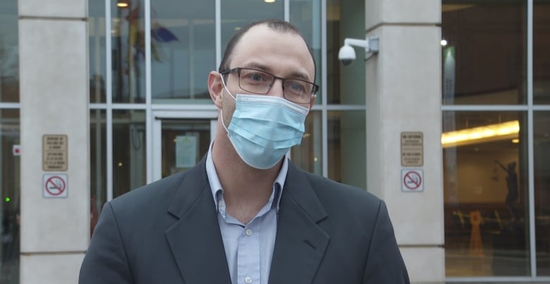 Man standing in front of a courthouse wearing a blue face mask. 