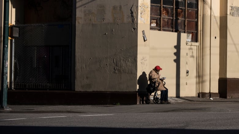 An elderly man on a wheelchair eats on a street corner.