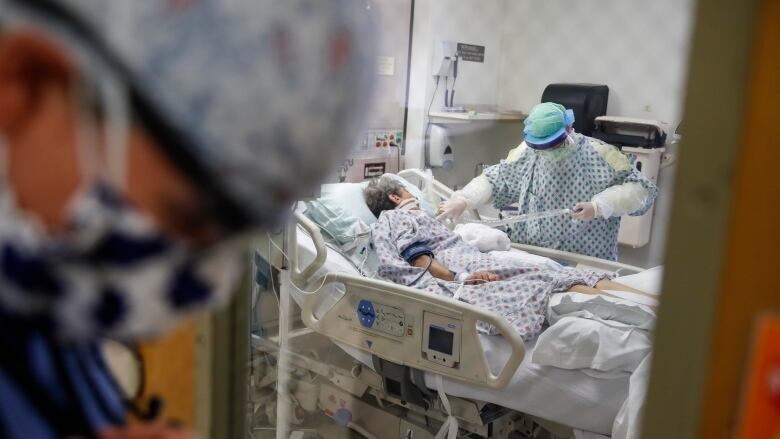 A resident physician stands outside a room at an intensive care unit as a nurse suctions the lungs of a COVID-19 patient.