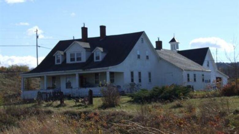 A sprawling white wooden building with a shingle roof is shown.