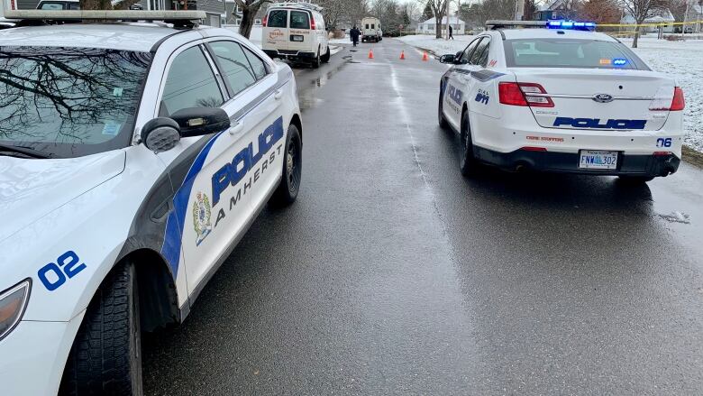 two Amherst police vehicles are parked in opposite directions on a paved street. there is snow on the ground. 