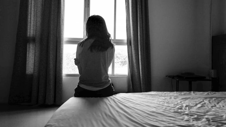 A woman sits on a bed in a black and white phot. Her face is not seen.