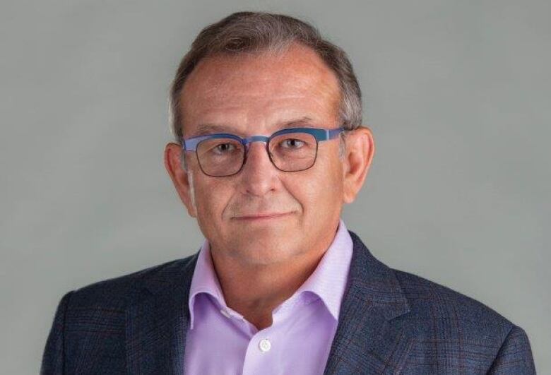 A man in a black blazer and purple shirt poses for a photo.