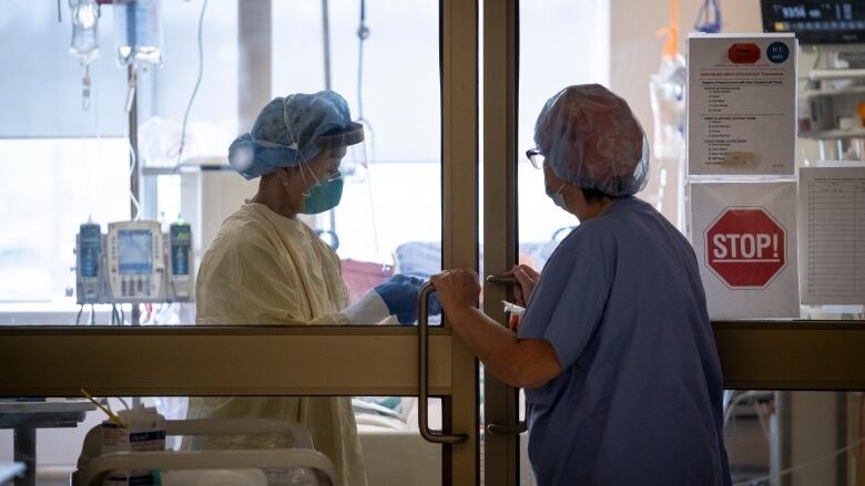 Medical staff talk through a glass door that's slightly open, both in full personal protective gear