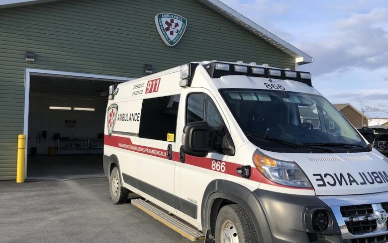 A white ambulance is parked at the bay of a green wooden building