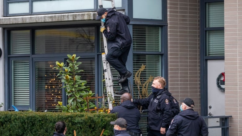 About half a dozen police officials investigating a crime scene with one climbing a ladder.