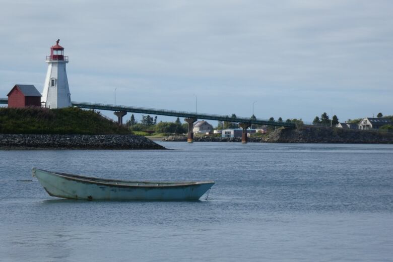 A lighthouse stands on the edge of the land with a bridge behind it.