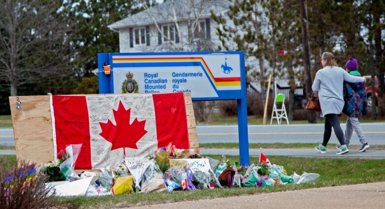 Photo of floral tributes and a signed Canadian flag in front of an RCMP sign.